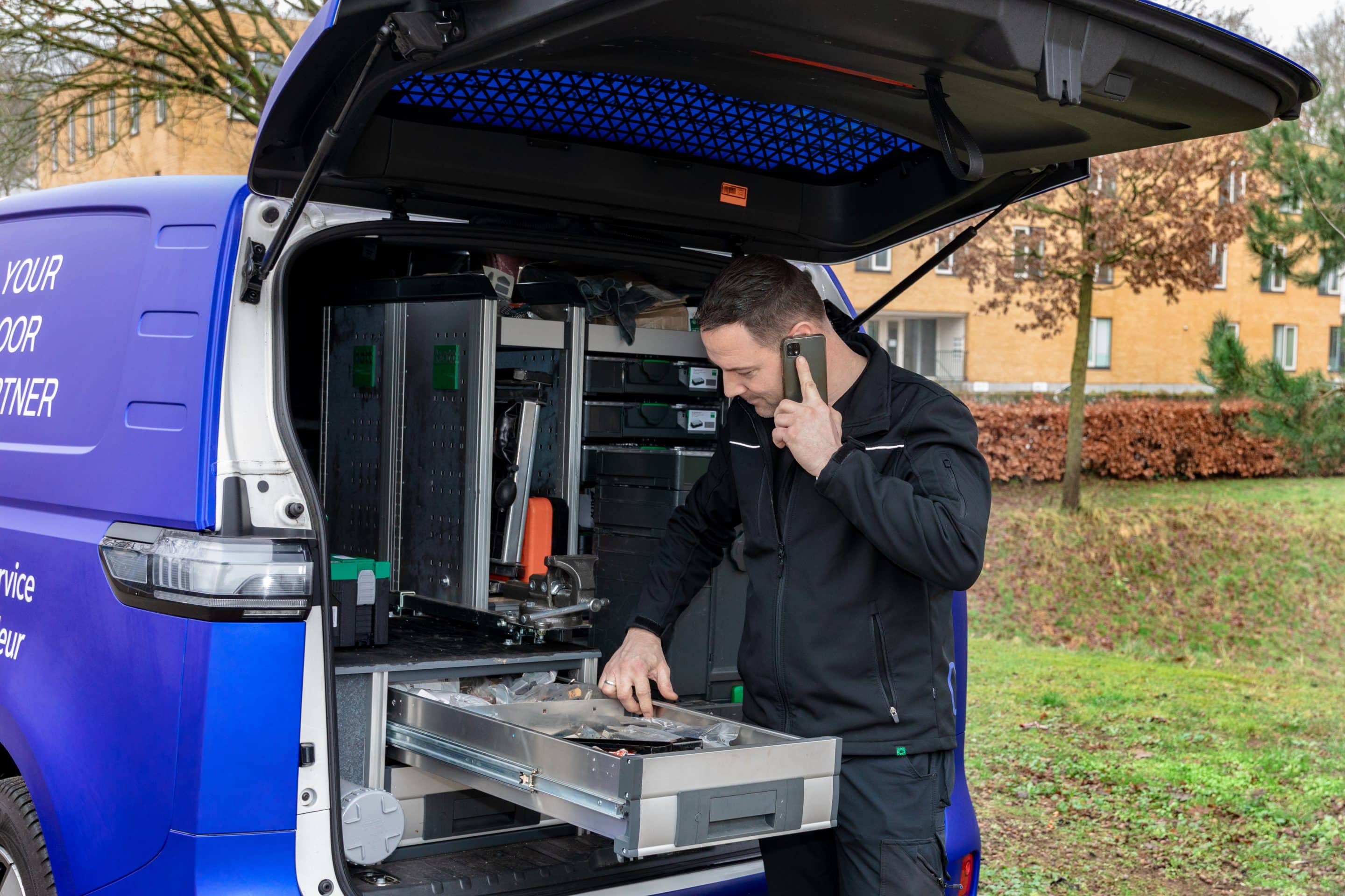 automatische-deur-storing-service.jpg Monteur met pak spullen uit de monteursbus terwijl hij belt